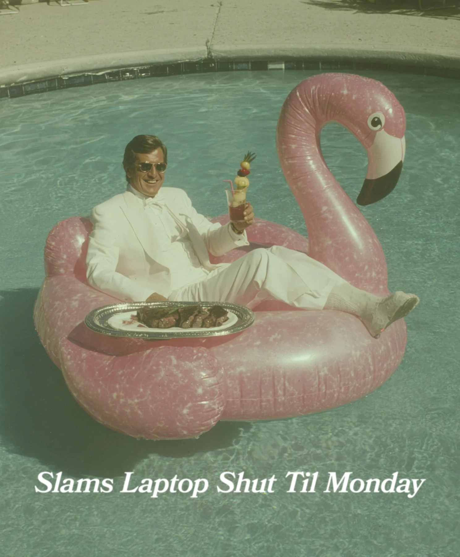 A man in a white suit and sunglasses relaxing on a pink flamingo pool float in a swimming pool. He is holding a drink garnished with fruit and has a tray of grilled food nearby. Text at the bottom reads, "Slams Laptop Shut Til Monday."