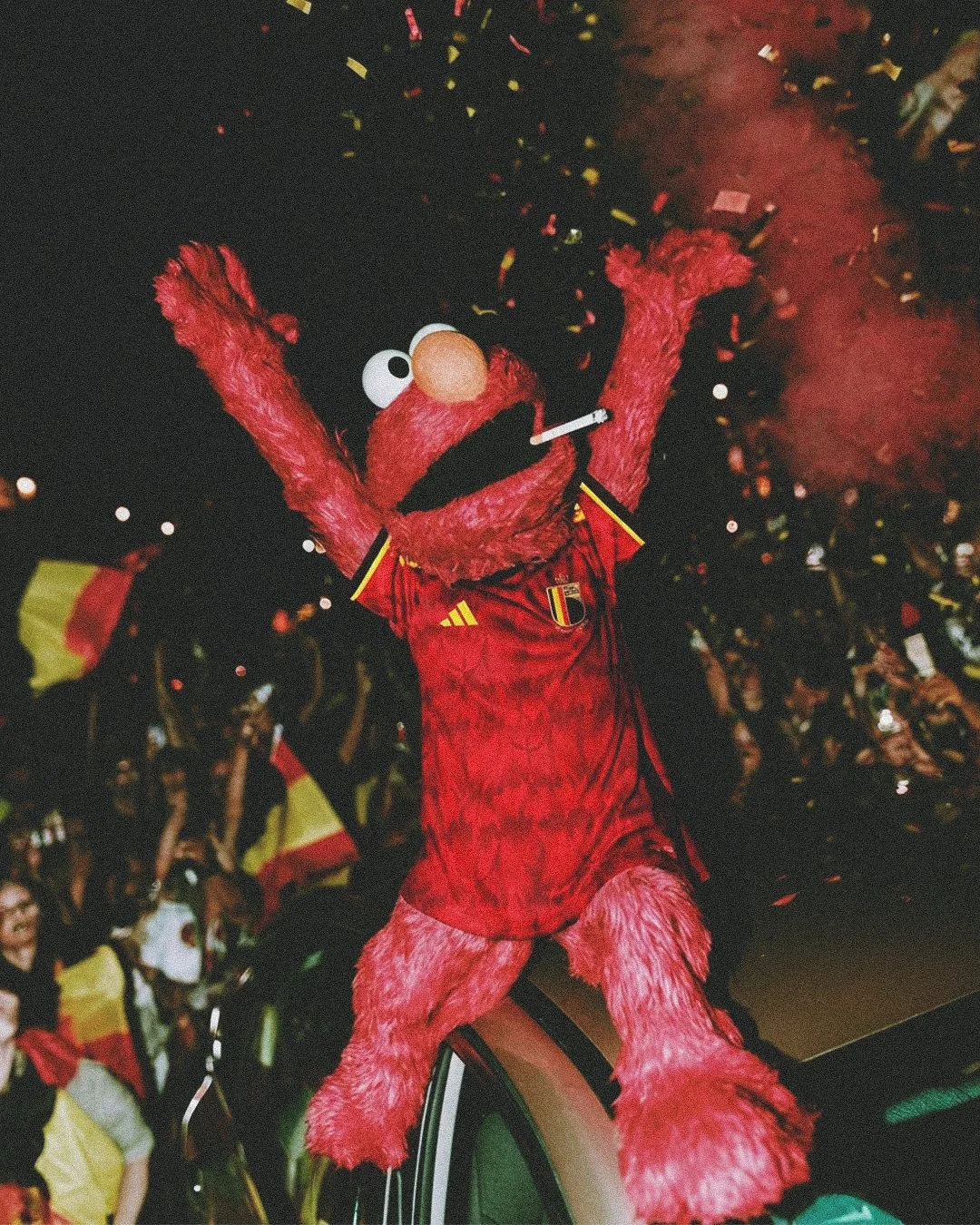 Elmo puppet dressed in a Belgium soccer jersey celebrating at a crowd filled with cheering fans.