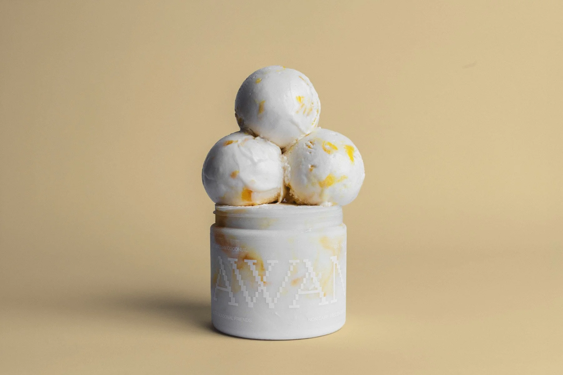Four scoops of ice cream with a white and yellow marbled pattern on top of a white container with a minimalistic design set against a beige background.