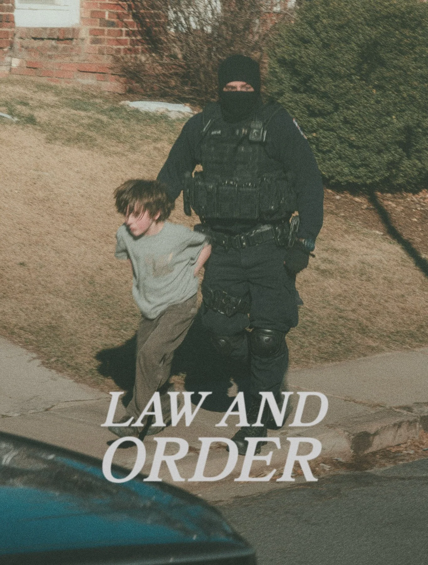 A police officer in tactical gear detaining a young man on the sidewalk at night. Text overlay reads 'LAW AND ORDER'.