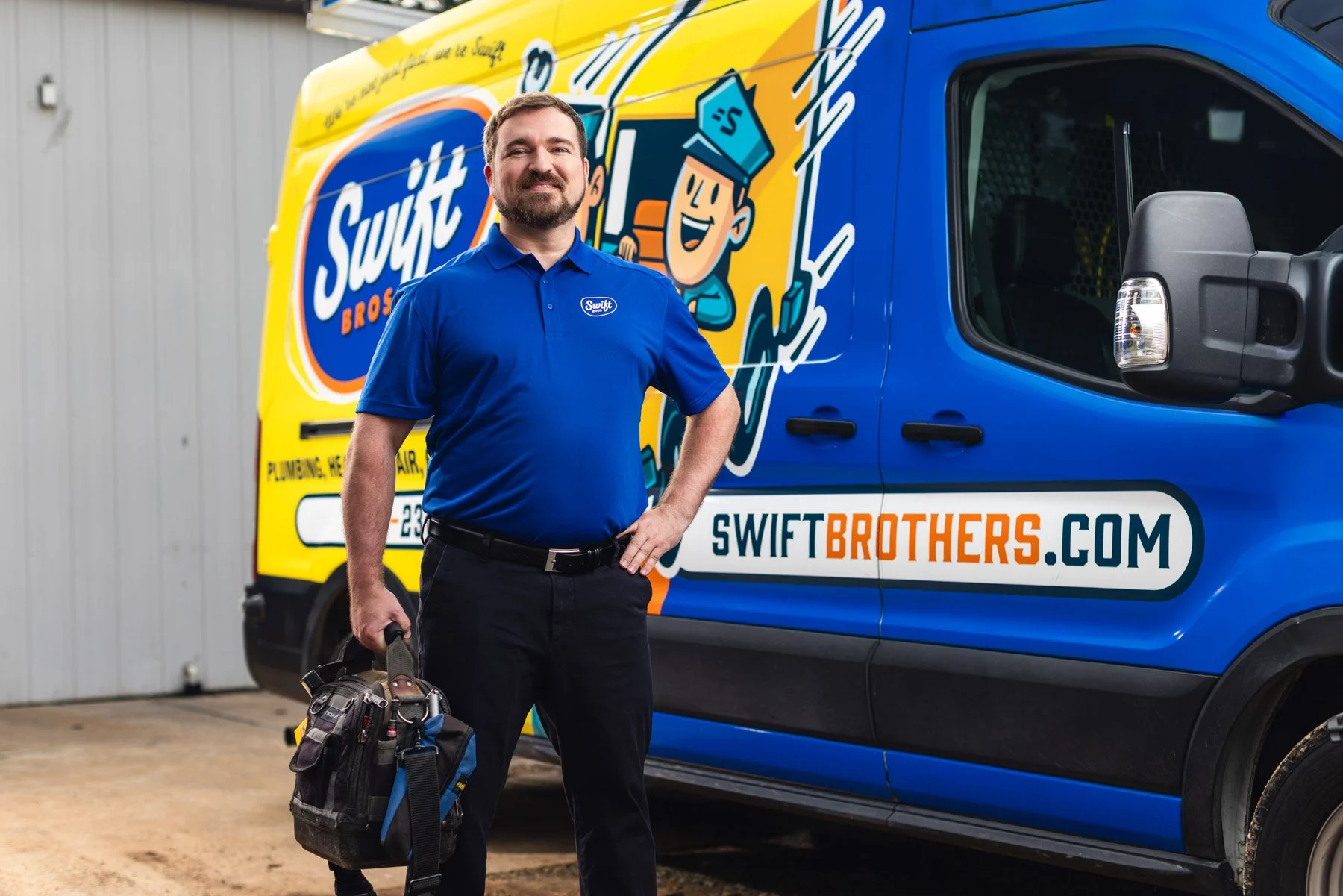 A man wearing a blue Swift Brothers uniform shirt stands in front of a bright blue and yellow Swift Brothers service truck, holding a tool bag and smiling.
