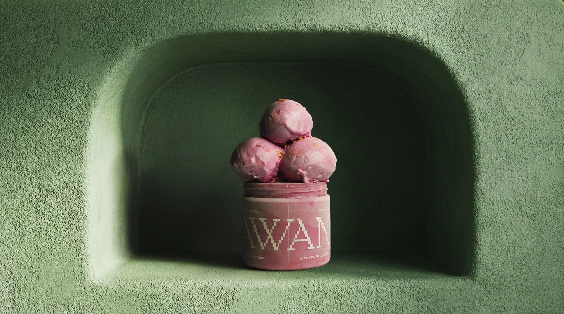A pink container of ice cream with three scoops on top, placed in a green niche in a textured green wall.