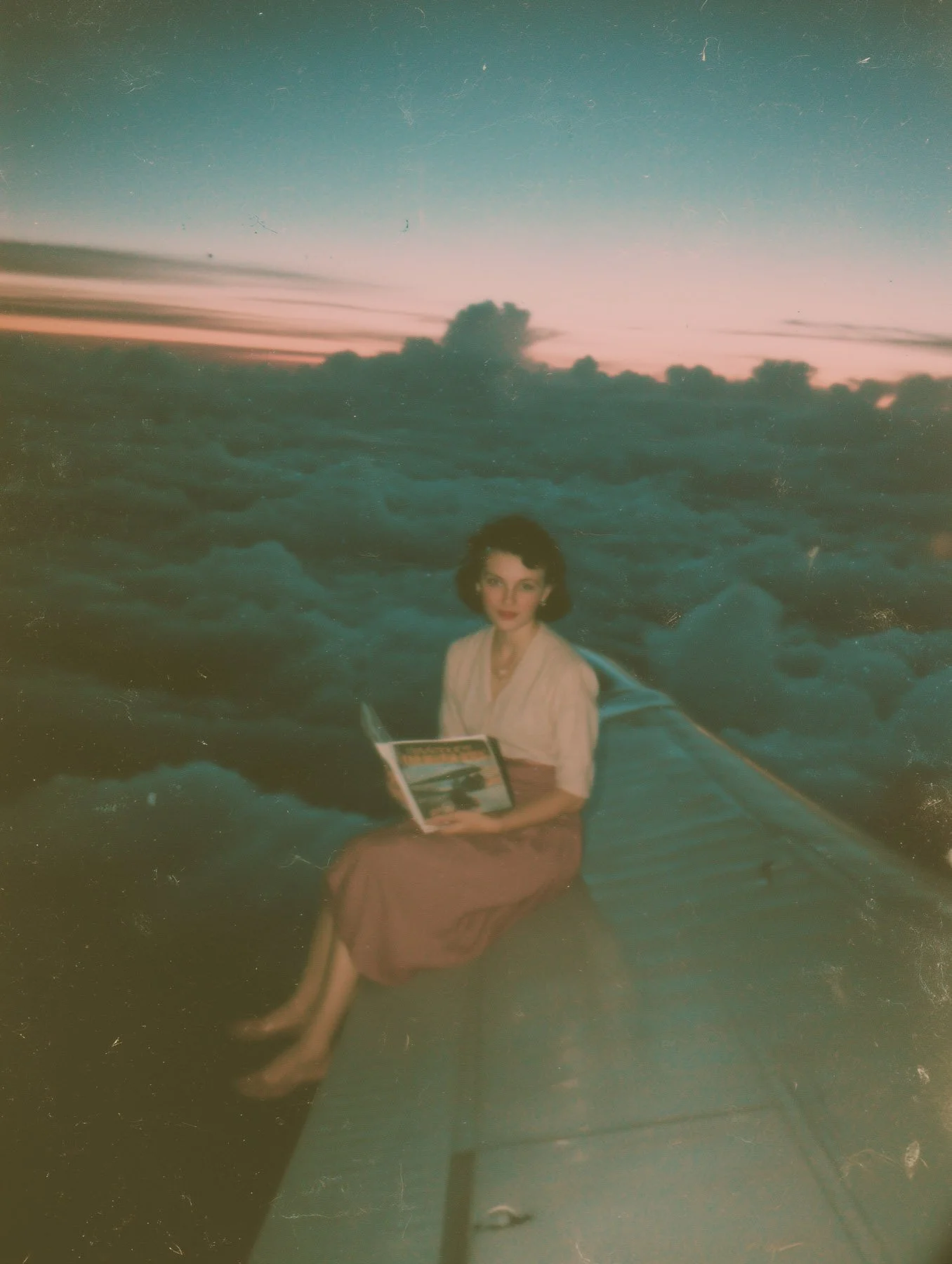 A woman sitting on a boat at sunset, holding a book and looking at the camera with clouds and a colorful sky in the background.