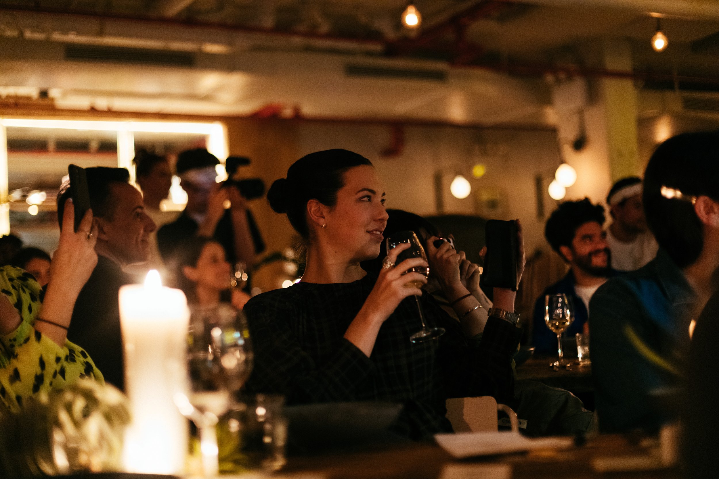 People enjoying a cozy indoor gathering, holding wine glasses, with dim lighting and candles.