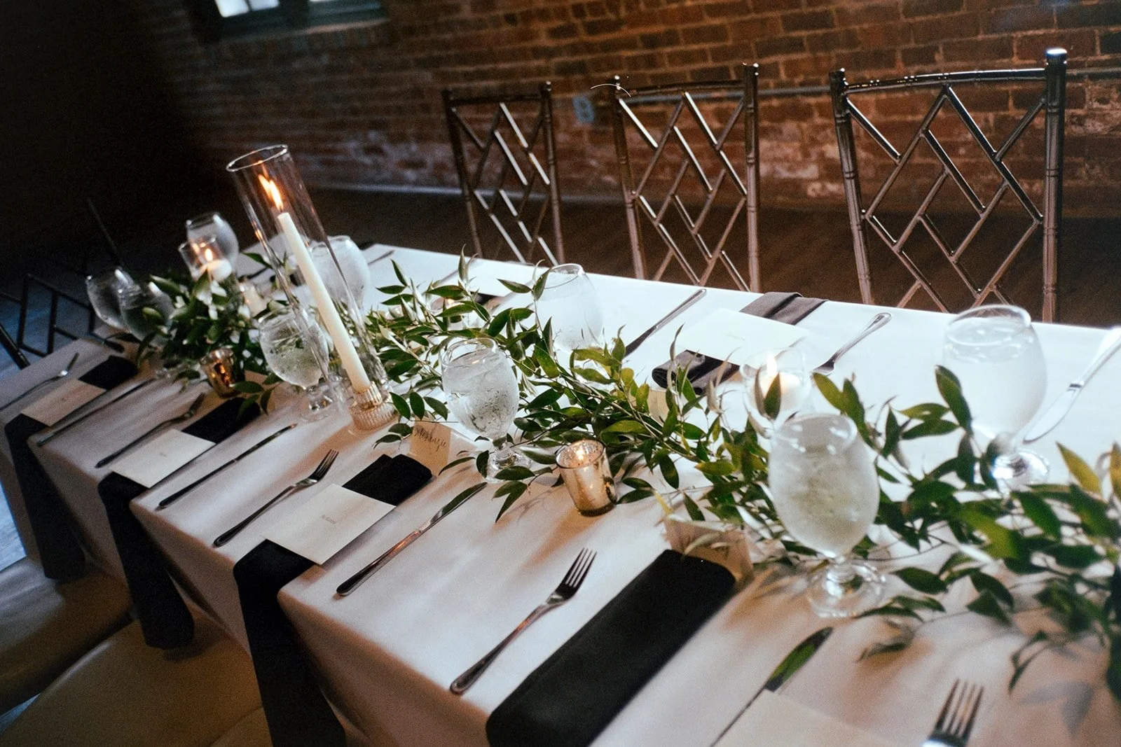 Table centerpiece at The L with greenery runner, taper candles, floating candles, and tea lights. 