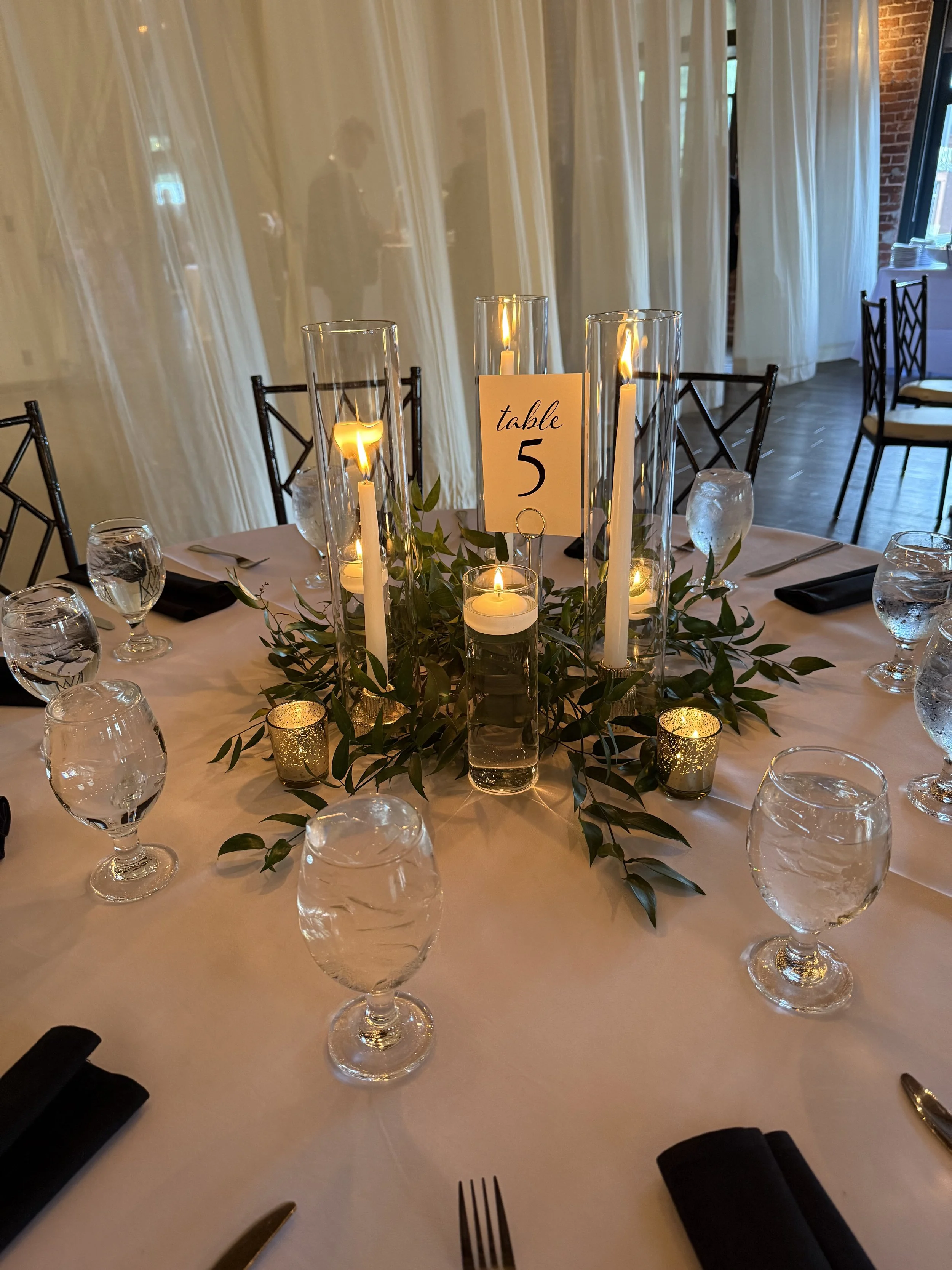 Greenery table centerpiece with taper candles & hurricanes, floating candles, and tea lights at The L. 