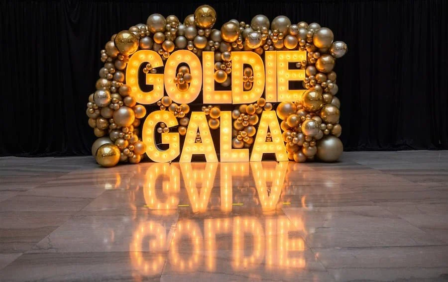 2025 in review - lit letters that spell out Goldie Gala with gold metallic balloons all around