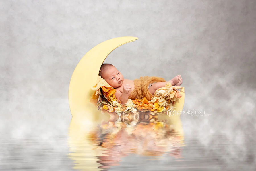 baby boy posing in moon prop during newborn baby photo session in Sydney studio
