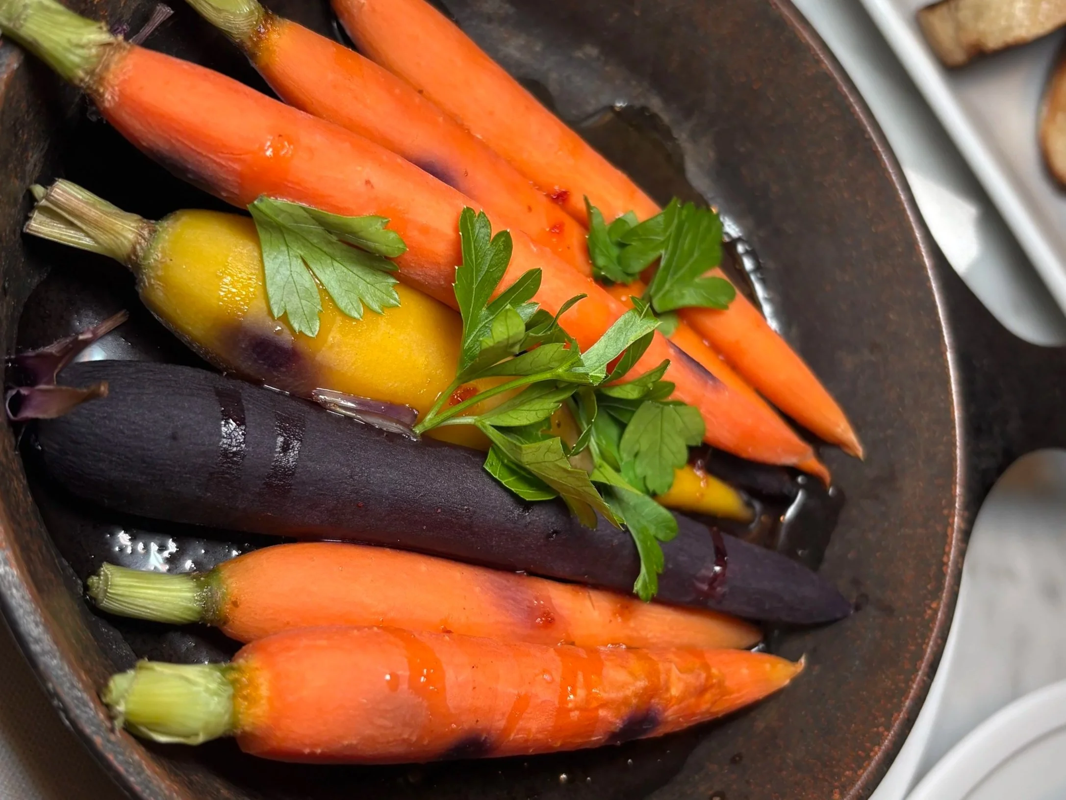 Colorful assortment of raw carrots and a yellow eggplant in a skillet, garnished with fresh parsley.