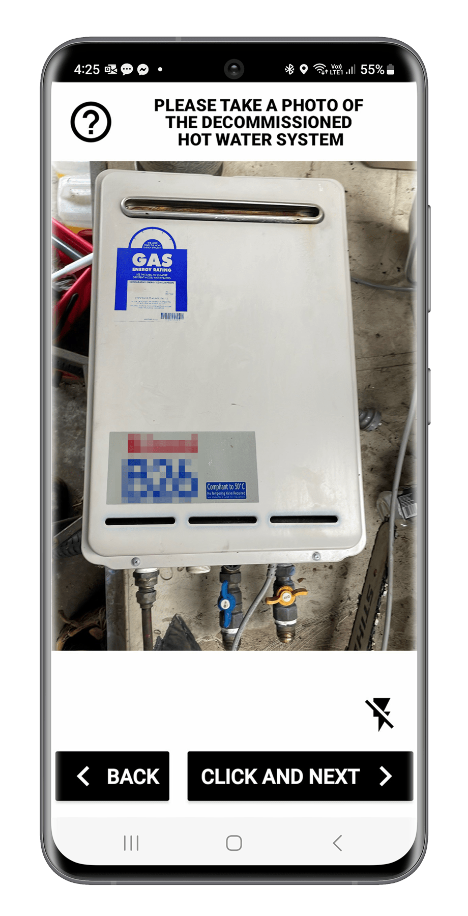 Photo of a decommissioned hot water system, a white rectangular unit with labels and valves, mounted on a concrete floor.