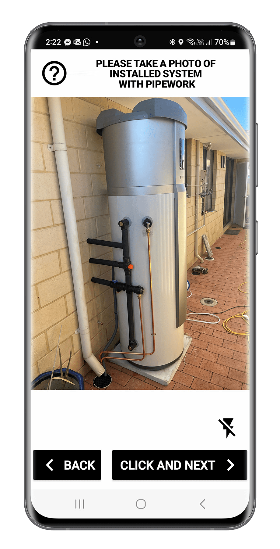 A water heating system installed outdoors on a brick patio, with pipes and access panels.