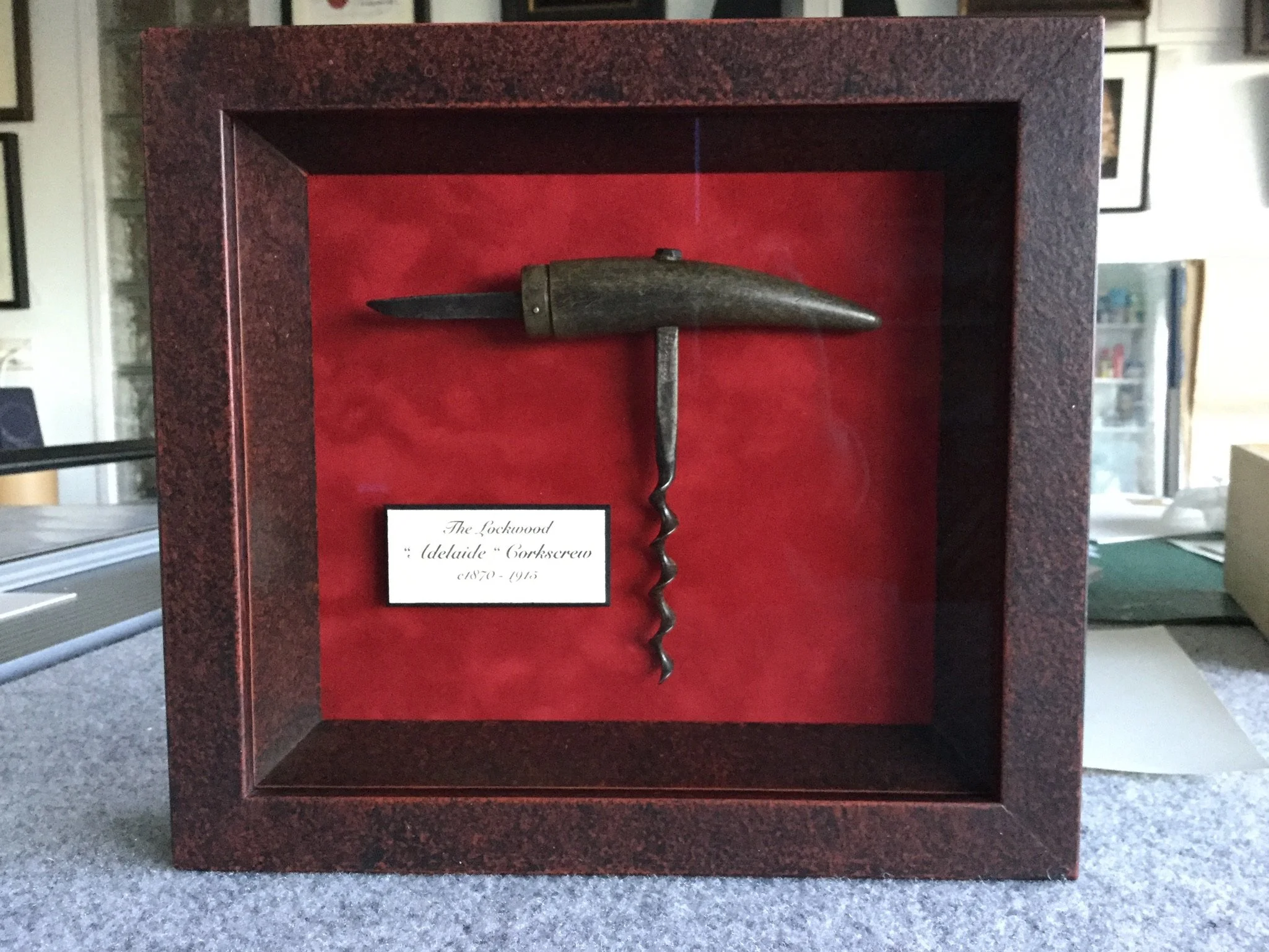 Vintage corkscrew and knife in a display case with red background, labeled as The Lockwood 'Adelaide' Corkscrew from 1870.
