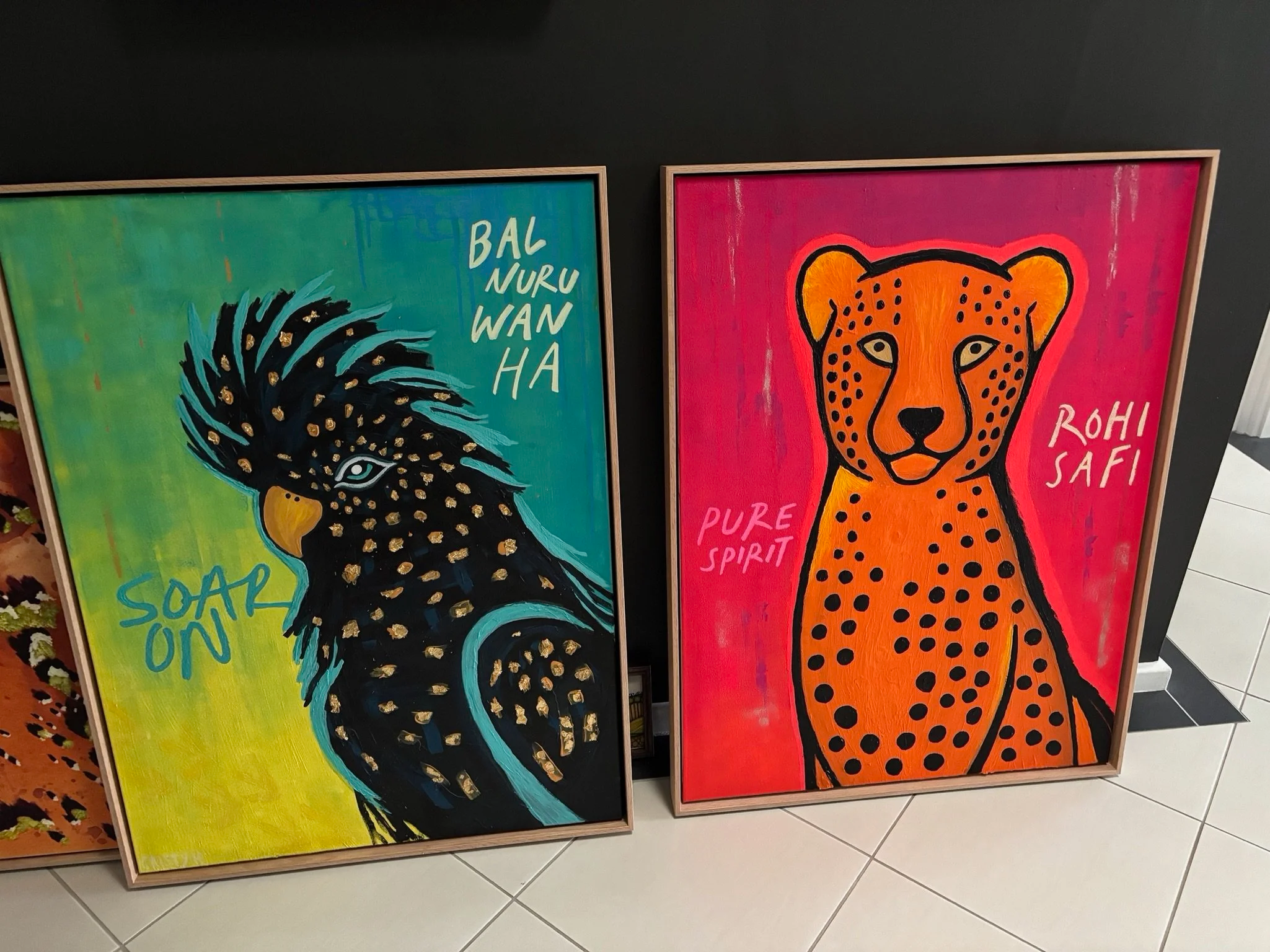 Two colorful animal paintings, one of a cockatoo with the words 'Bal Nuru Wanha' and 'Soap On,' and the other of a cheetah with the words 'Pure Spirit' and 'Rohi Safari'.