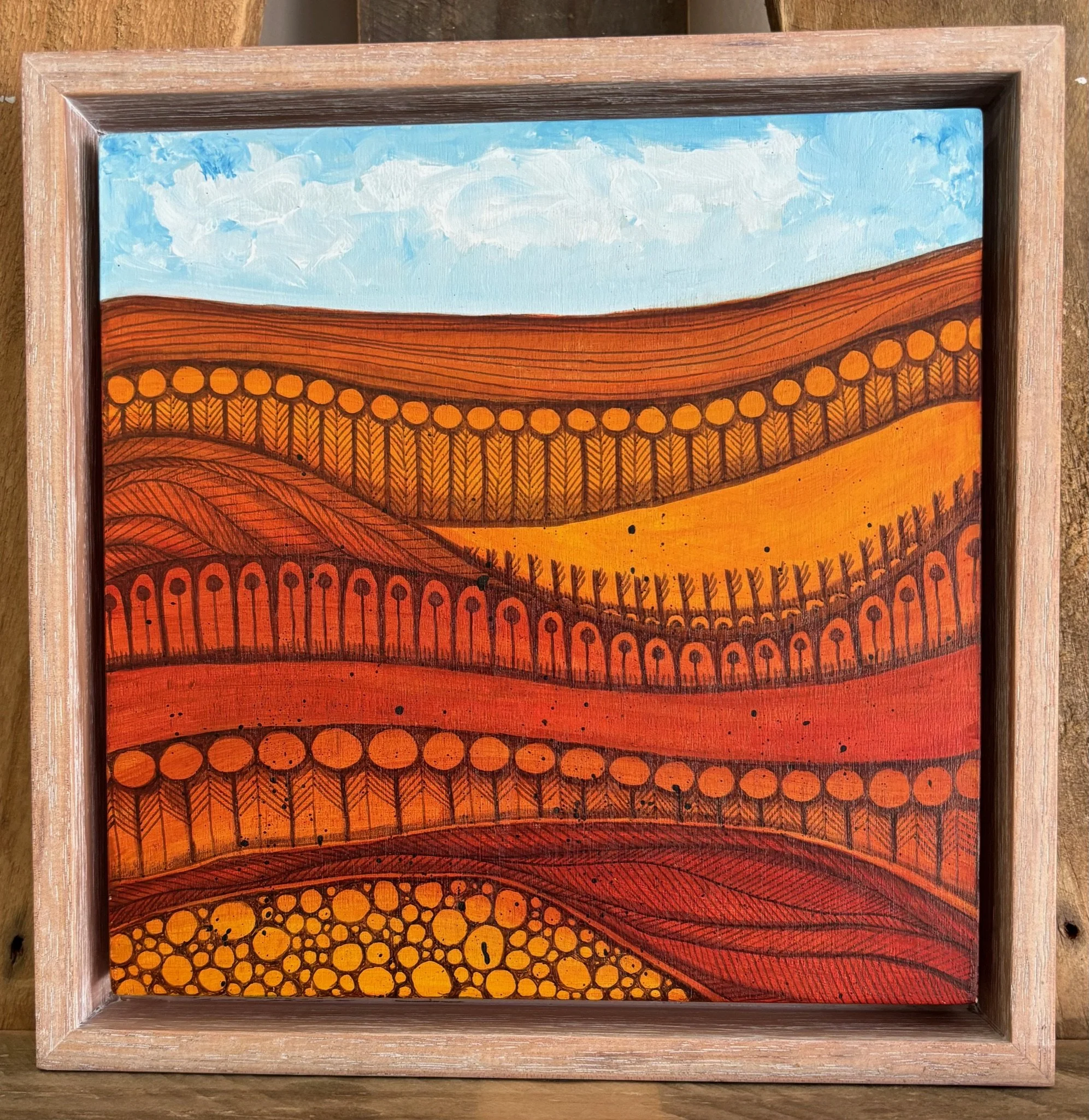 A colorful landscape painting of rolling hills in warm shades of red, orange, and yellow, with stylized trees and patterns, under a light blue sky with wispy clouds.