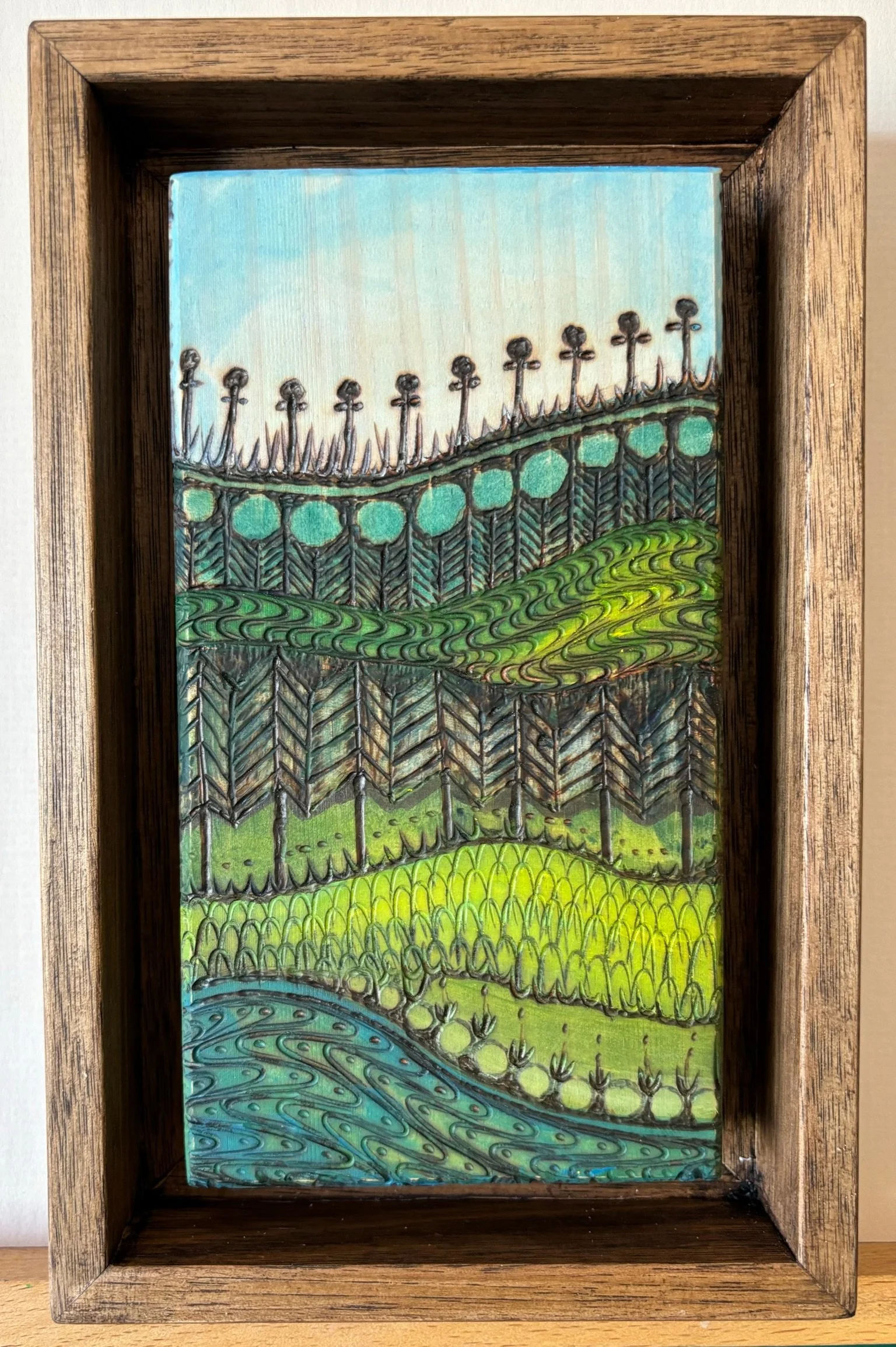 Colorful abstract landscape painting of hills, trees, grass, and a river, framed in wood.