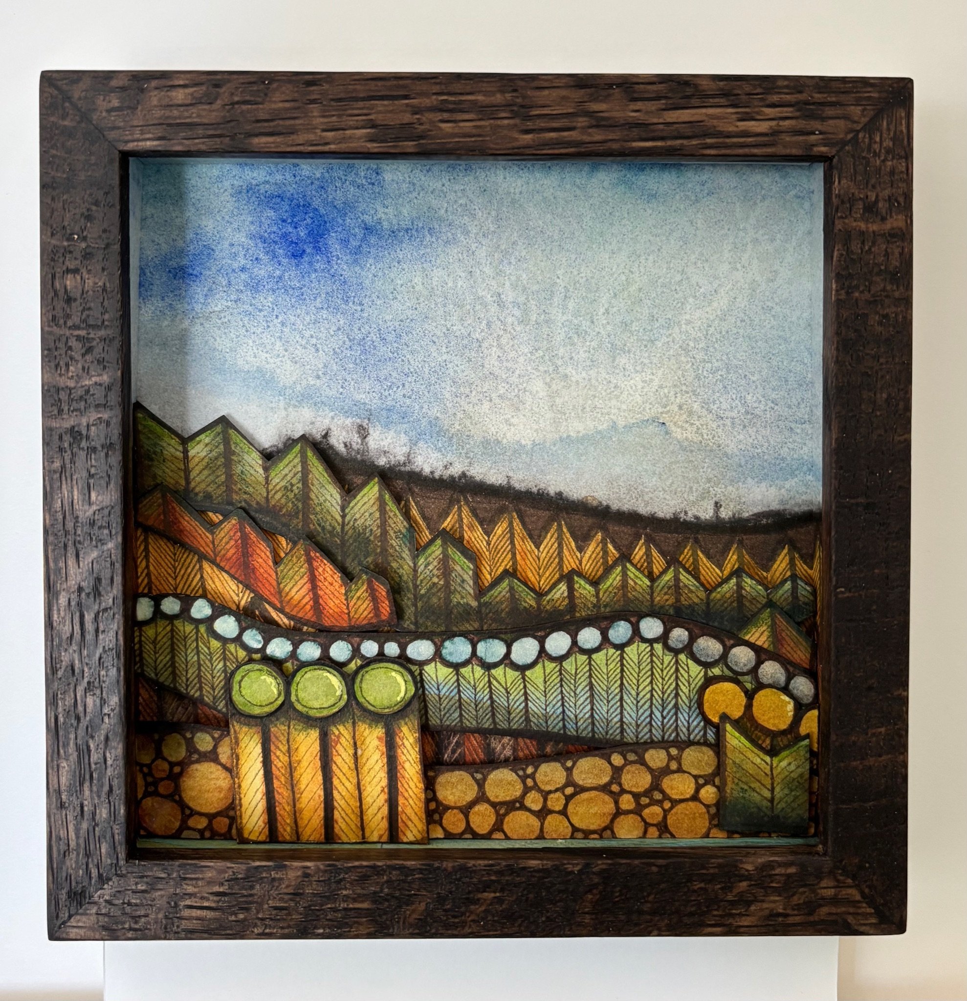 Colorful landscape art with geometric trees, hills, and sky inside a wooden frame.