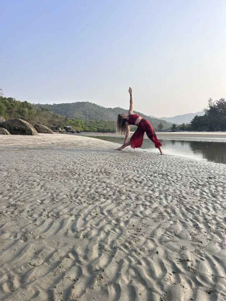 Woman doing yoga on sandy beach near water with mountains in the background during daytime.
