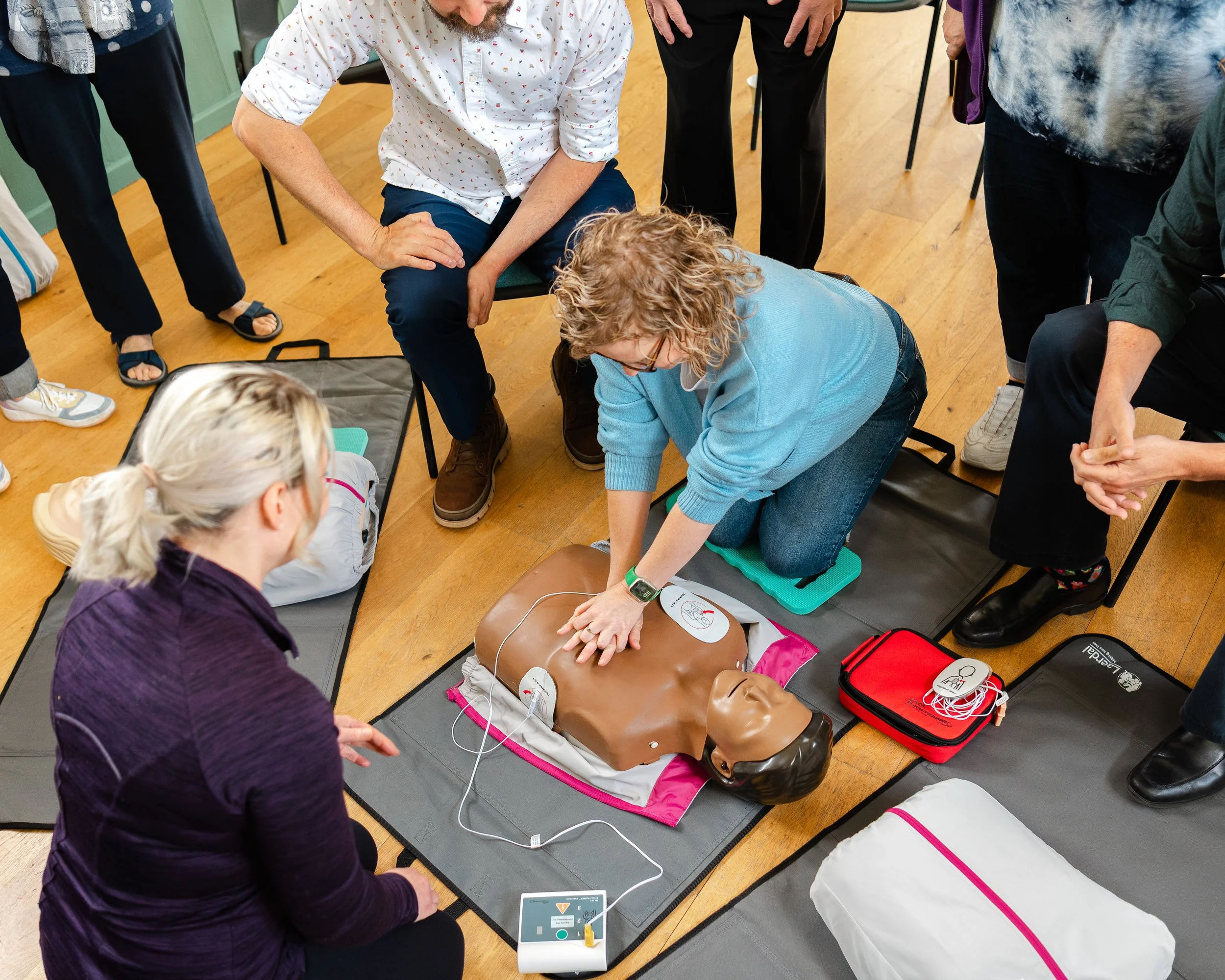 Group of people practicing CPR on a mannequin during a training session, with medical equipment nearby.