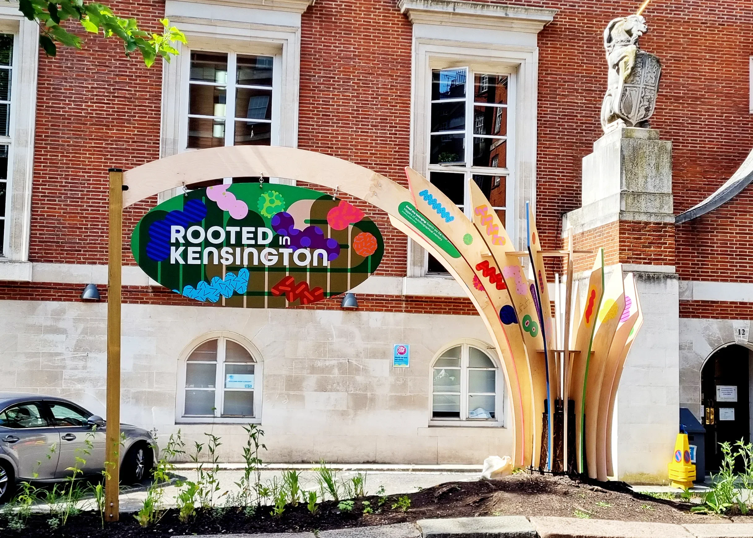 'Rooted in Kensington: Tree Island' public art by MAMIMU and Toy Studio with colorful shapes inspired by biodiversity and microbiome, set against a brick building background.