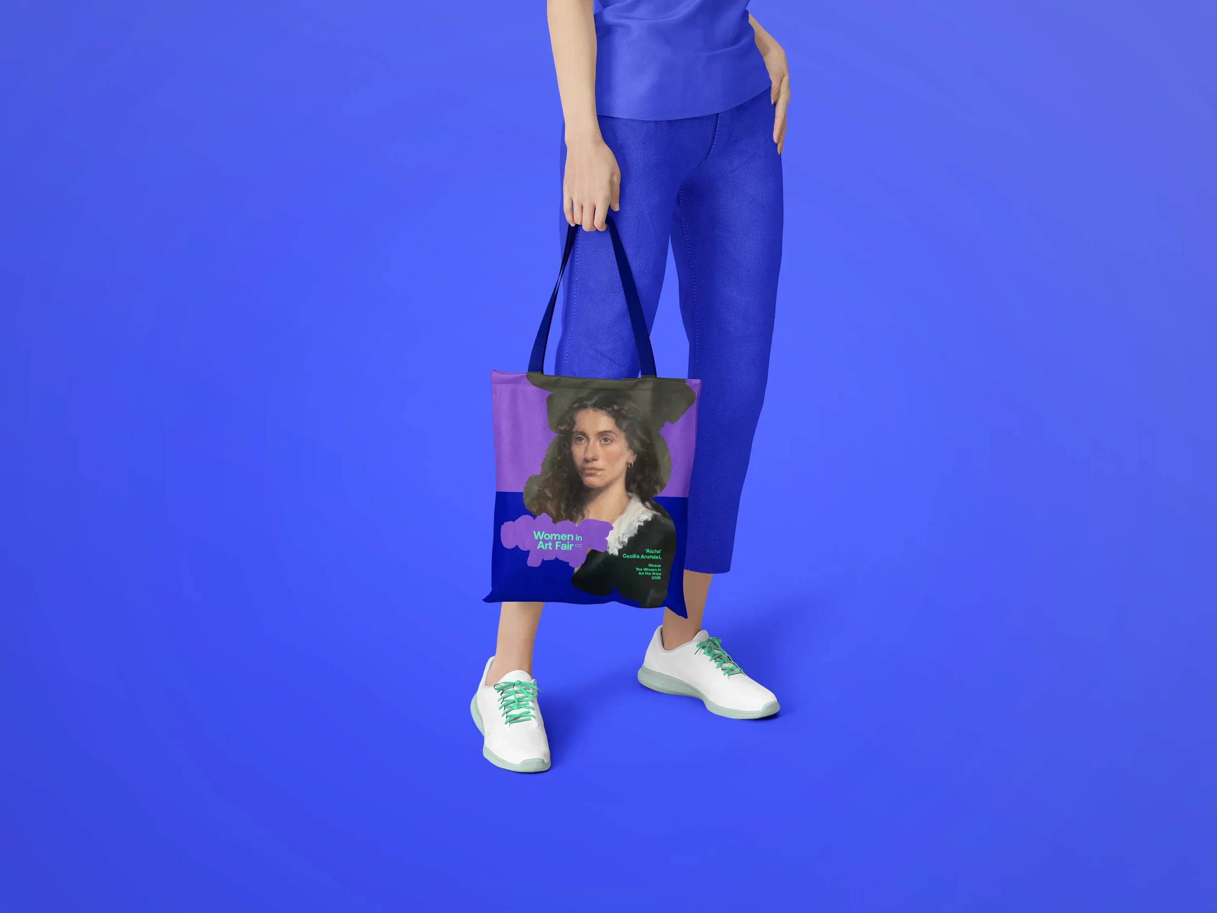 A women standing on a blue background holding a tote bag with a portrait of a woman and event information for Women in Art Fair.
