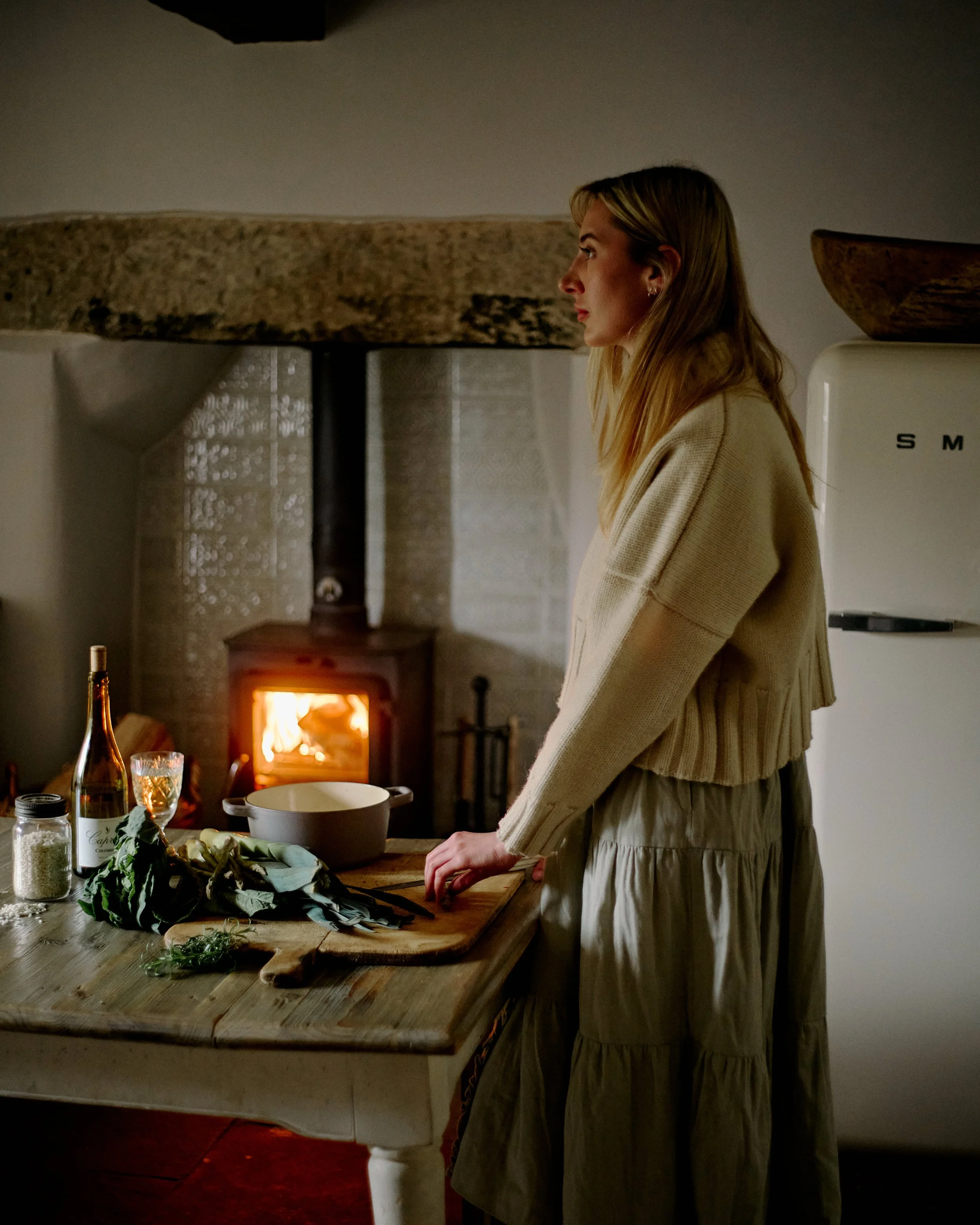 woman preparing food at farmhouse table in front of fire
