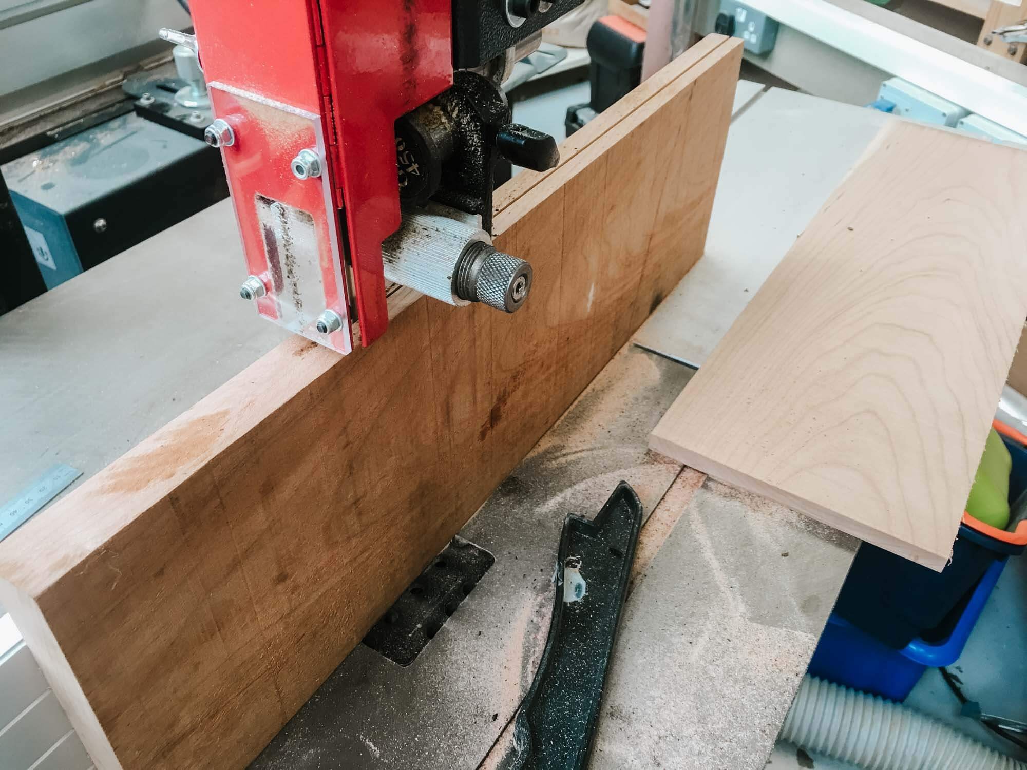A bandsaw cutting through a wooden board in a workshop, with sawdust scattered around.