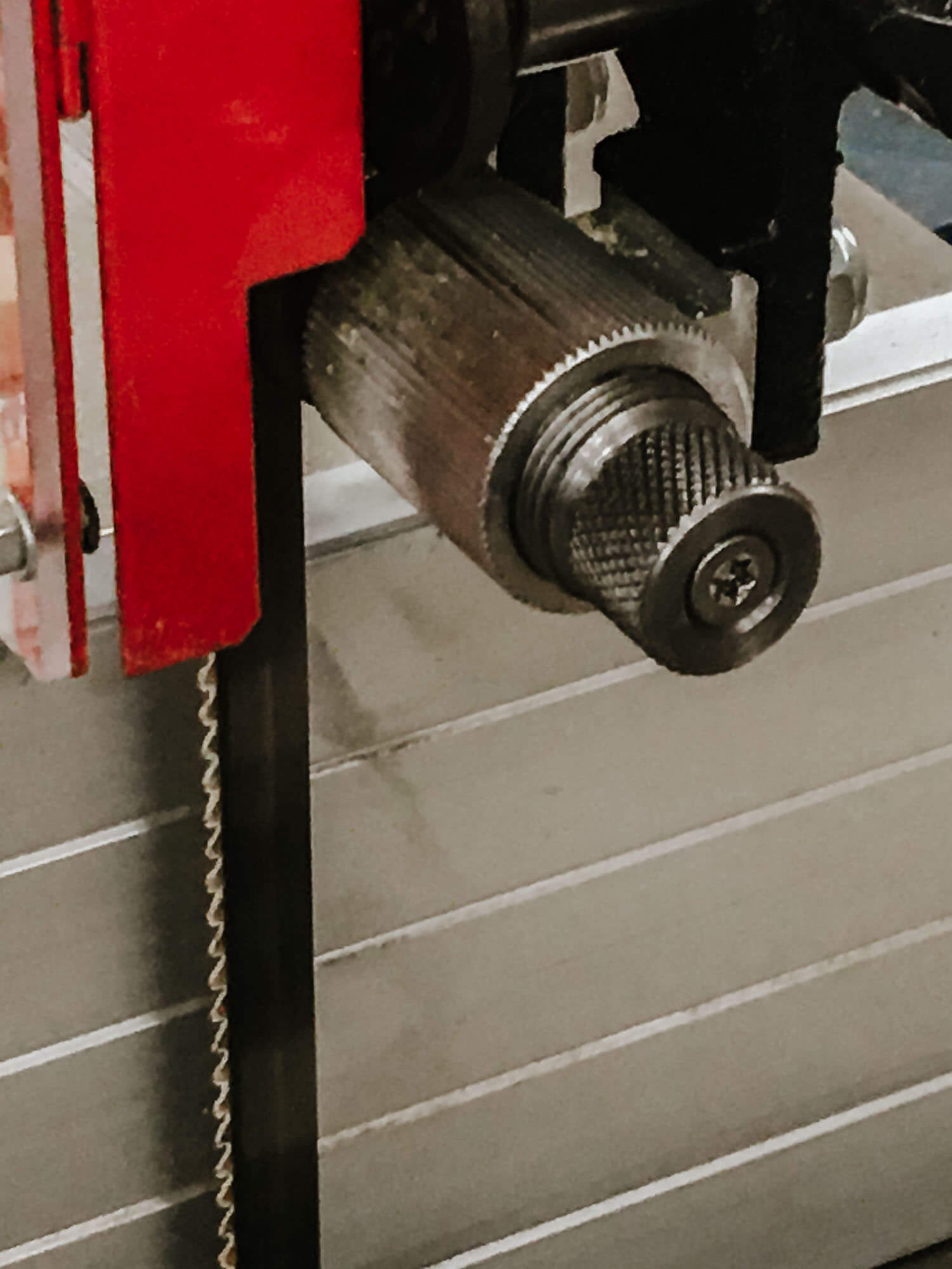 Close-up of a bandsaw blade tensioner, featuring a red guard and a metal knob used to adjust tension.
