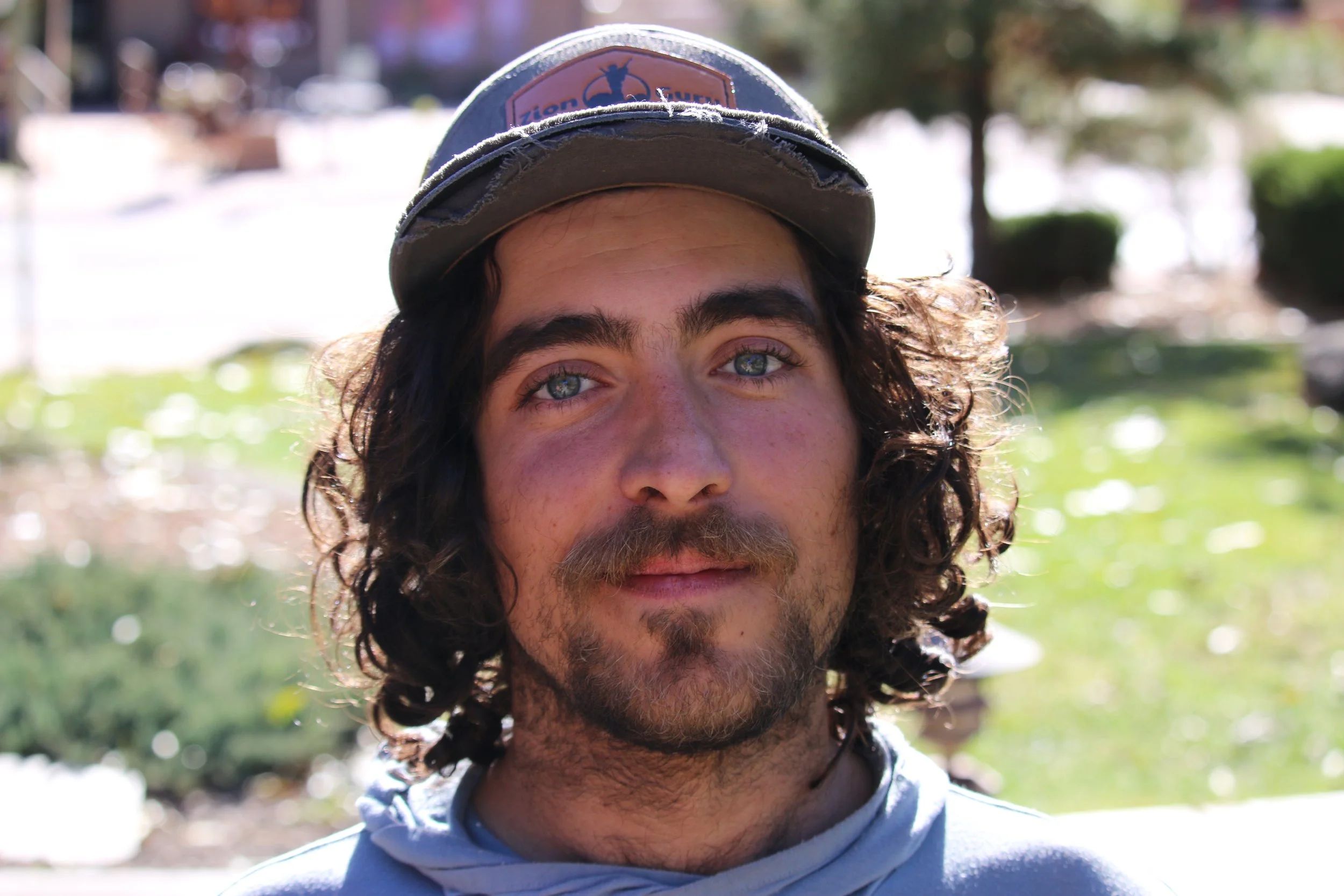 Close-up of a man with curly hair wearing a cap outdoors