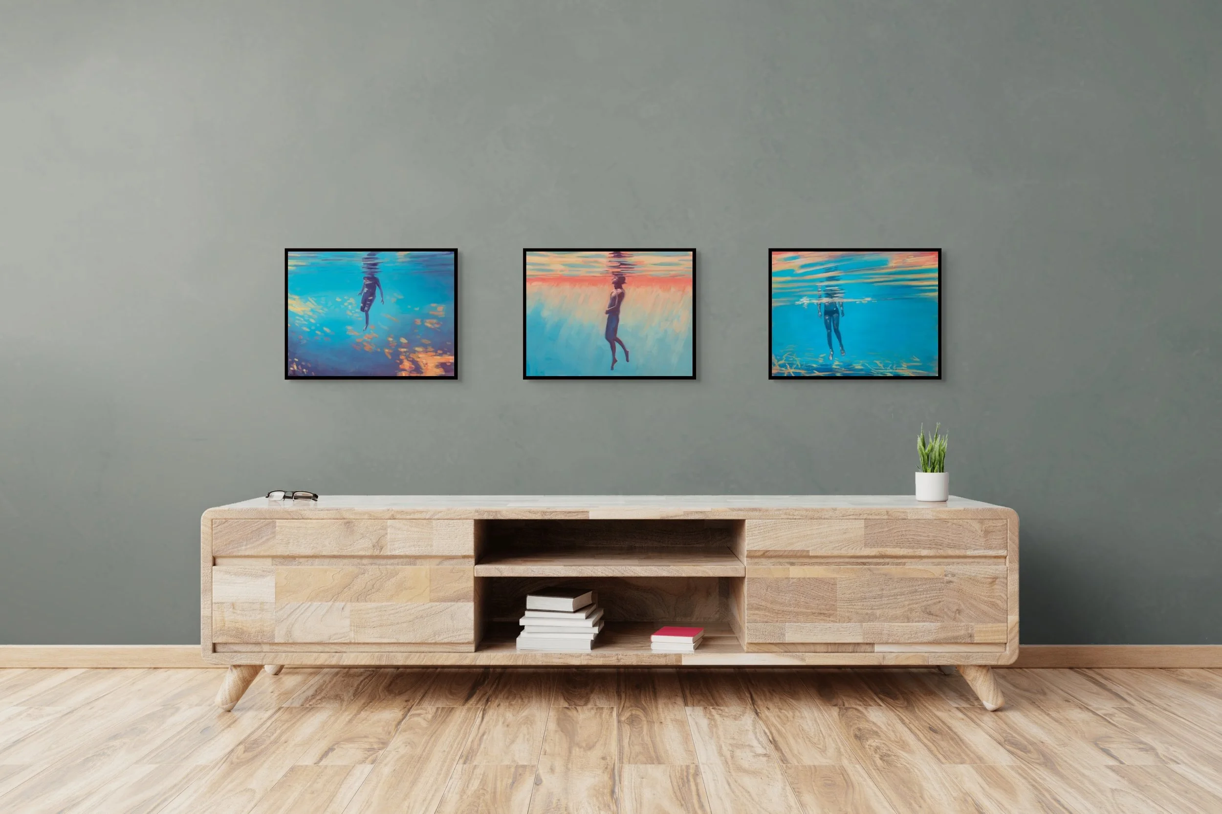 Living room with three framed underwater photographs on a gray wall, a wooden console table with books, a white pot with a green plant, and wooden flooring.
