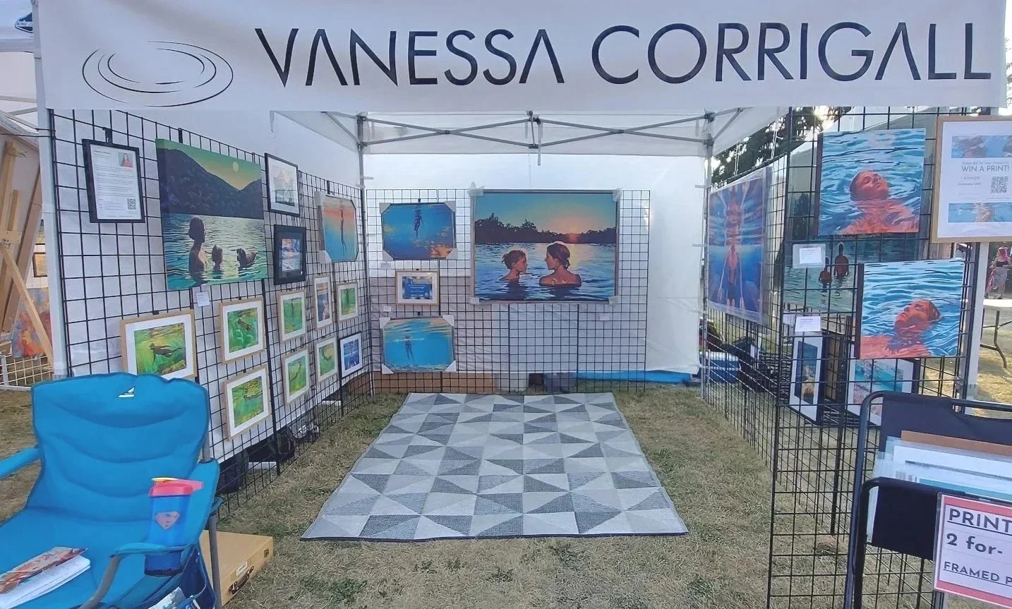 Vanessa Corrigall art booth at Strathearn Art Walk in Edmonton featuring underwater swimmer paintings, framed artwork, and print display inside outdoor festival tent