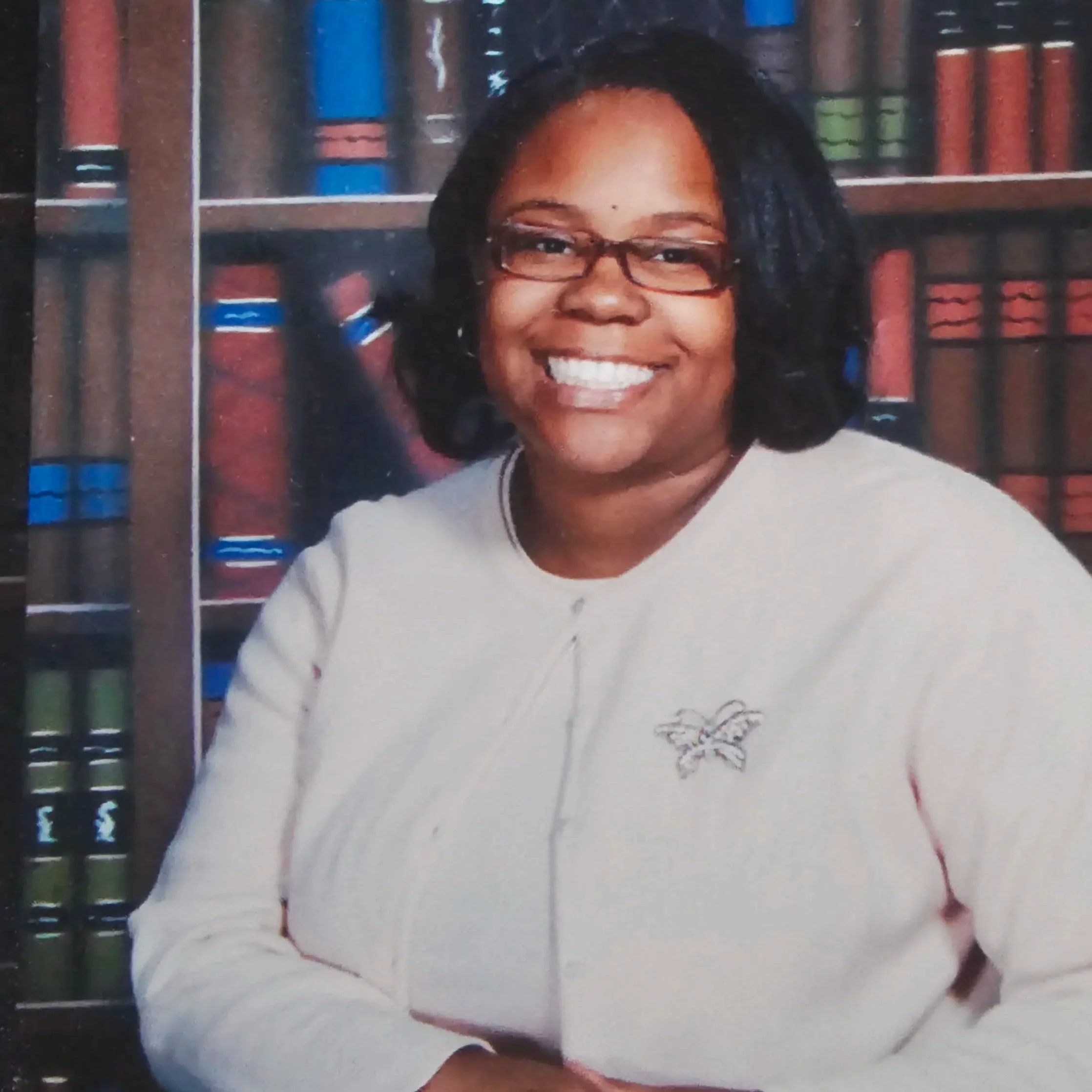 head shot of woman in white top in front of bookshelf