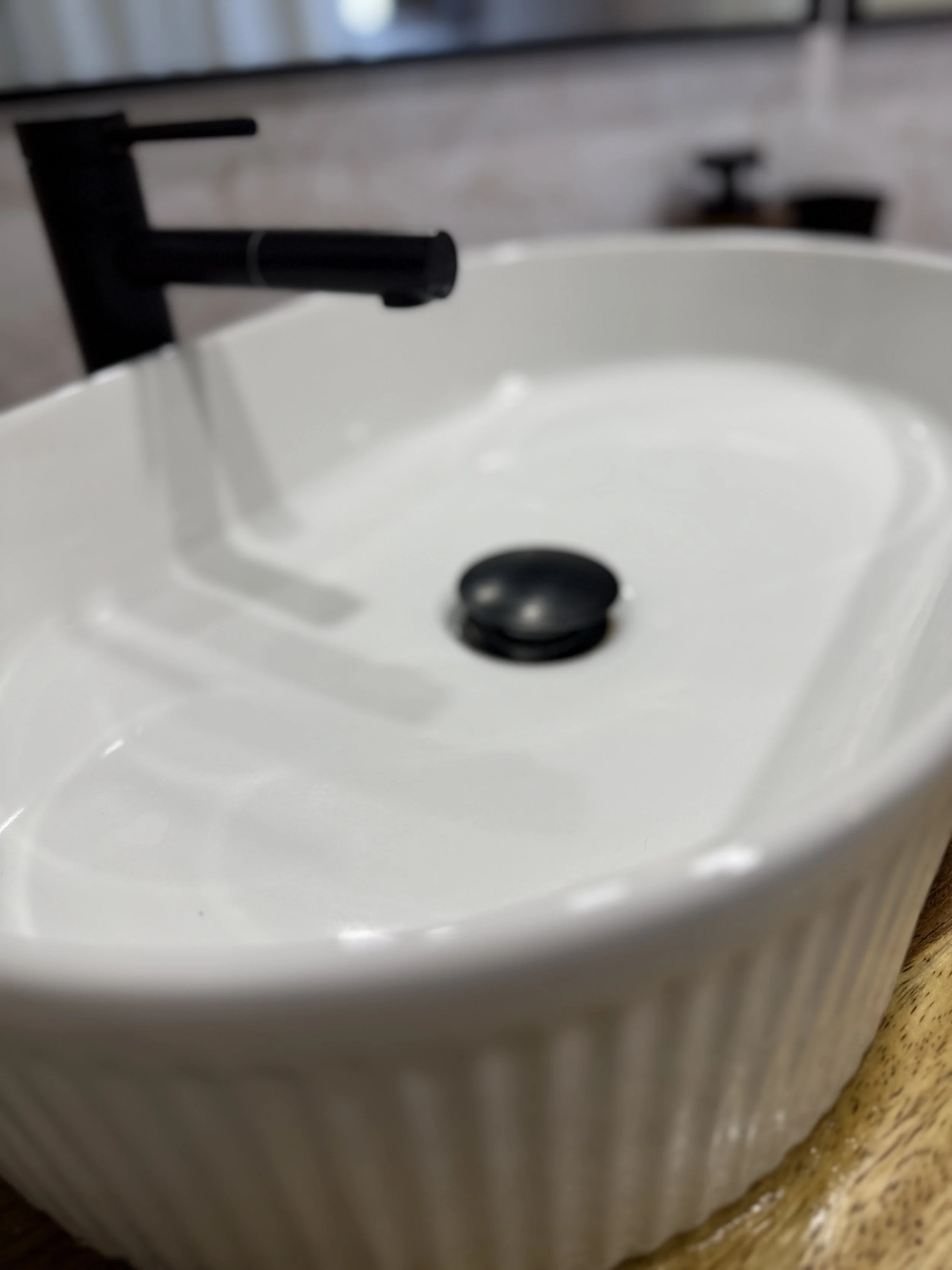 Porcelain bathroom sink with a black faucet and drain stopper.