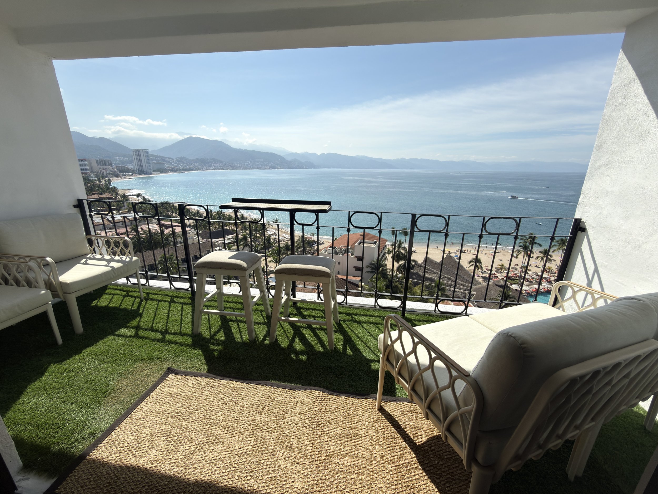 Balcony with outdoor furniture overlooking a beach and ocean with mountains in the background.