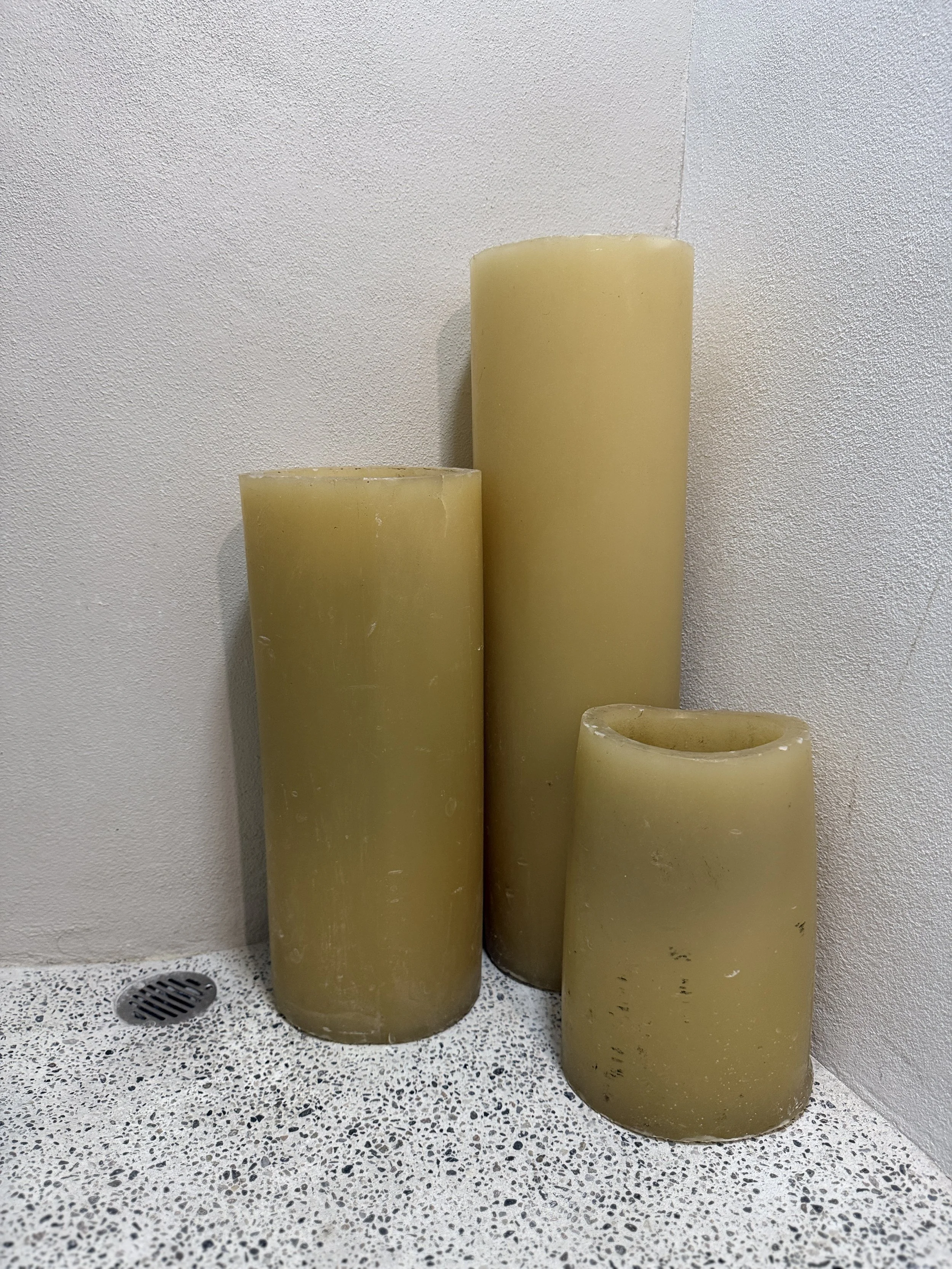 Three large yellow candles of varying heights placed on a speckled countertop near a wall.