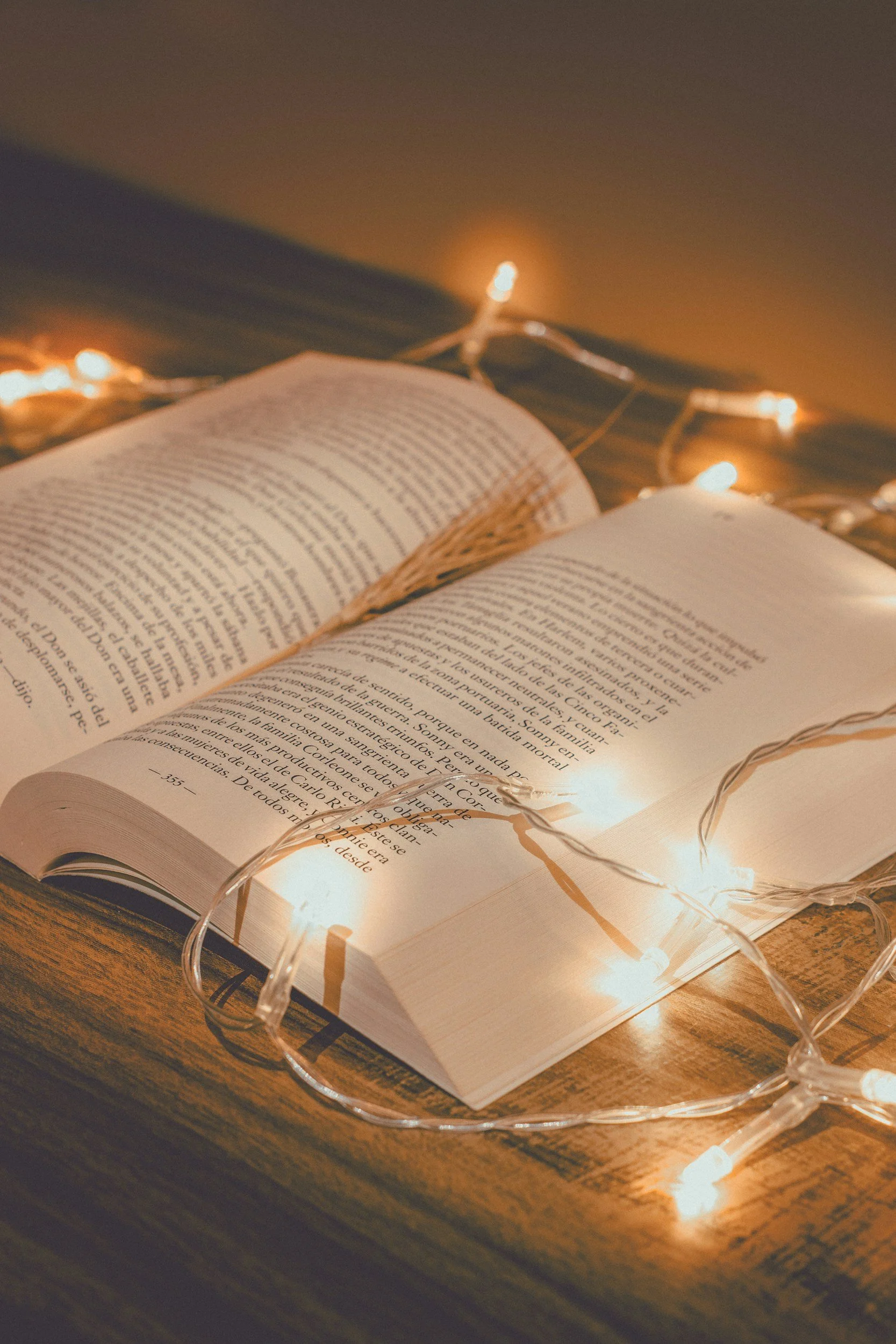 A desk with an open book and fairy lights draped across it.