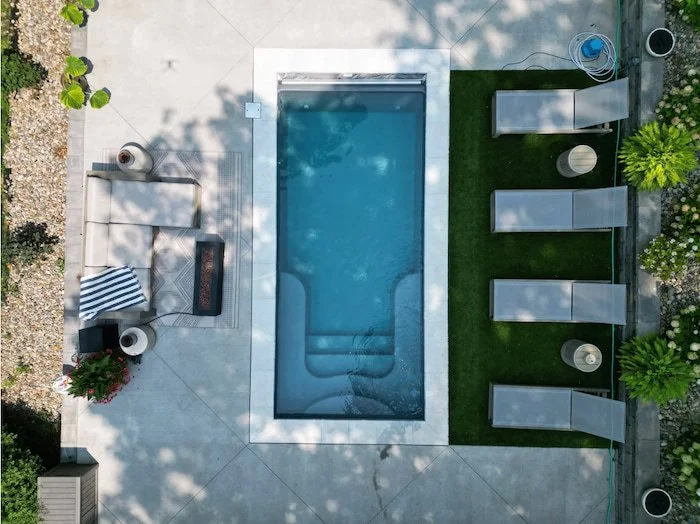 Aerial view of a compact Thursday Pools Sea Turtle fiberglass inground pool with ice coping stones, a turf side yard, and a concrete patio.