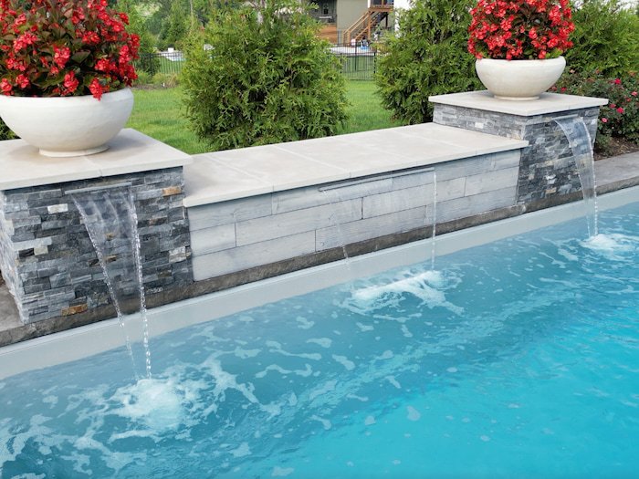 Close-up detail of a 14-foot stone veneer water feature wall with cascading waterfalls and decorative planters, installed by Tiger Pool and Patio as part of a Thursday Pools Goliath 16x37 fiberglass pool project in Kansas City.