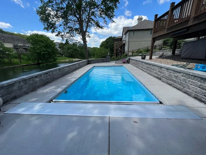 Thursday Pools Aspen 12x25 fiberglass inground pool in Caribbean Sparkle with an automatic safety cover and stone retaining wall, installed by Tiger Pool and Patio in Kansas City.