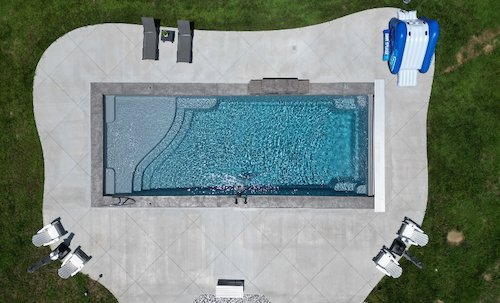 Aerial view of a Tiger Pool and Patio inground pool installation in KS—Thursday Pools Aspen 16x40 in Diamond with automatic safety cover, sheer descent waterfall, and basketball goal.