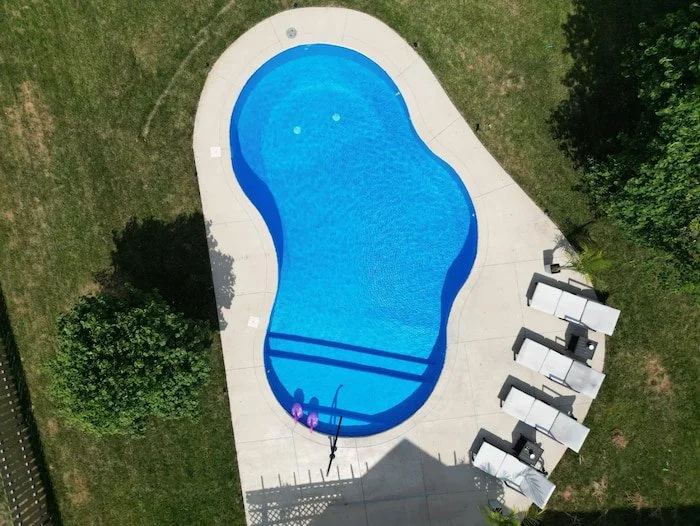Completed fiberglass pool installation in Kansas City showing 20x30 Mountain Lake design with a vibrant Merlin Blue Quartz vinyl liner, full-length sun deck, and black artisan handrail in residential backyard.