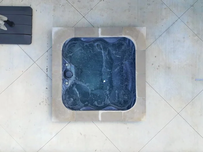 Overhead view of a 12-jet square fiberglass spa set into travertine pavers, part of a Thursday Pools Goliath 16x37 inground pool installation by Tiger Pool and Patio in Kansas City.