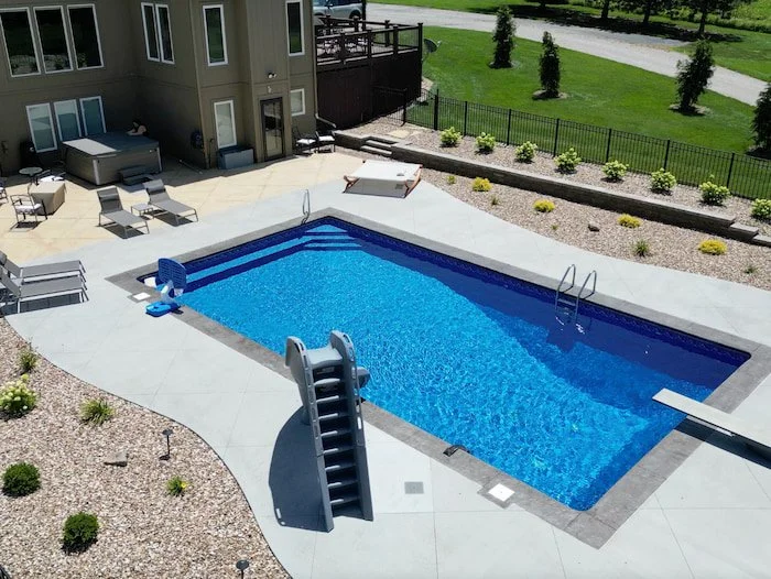 Custom inground pool design showcasing Tiger Pool and Patio's craftsmanship with 18x40 Diver model, 8-foot diving depth, dramatic Typhoon slide entry, GLI Cayman liner in Mystic Light Blue, corner steps with full bench seating, and relaxing hot tub i