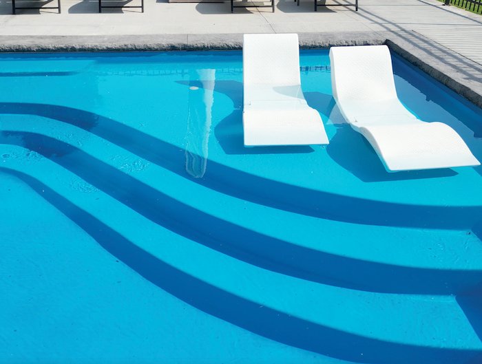 Close-up of the tanning ledge on a Thursday Pools Aspen 16x40 fiberglass inground pool in California Blue with in-water lounge chairs—a popular inground pool feature installed by Tiger Pool and Patio in Kansas City.