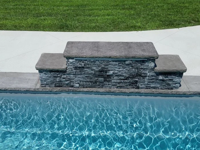 Close-up detail of a 4-foot sheer descent waterfall with stacked stone veneer surround cascading into a Thursday Pools Aspen 16x40 fiberglass inground pool in Diamond.