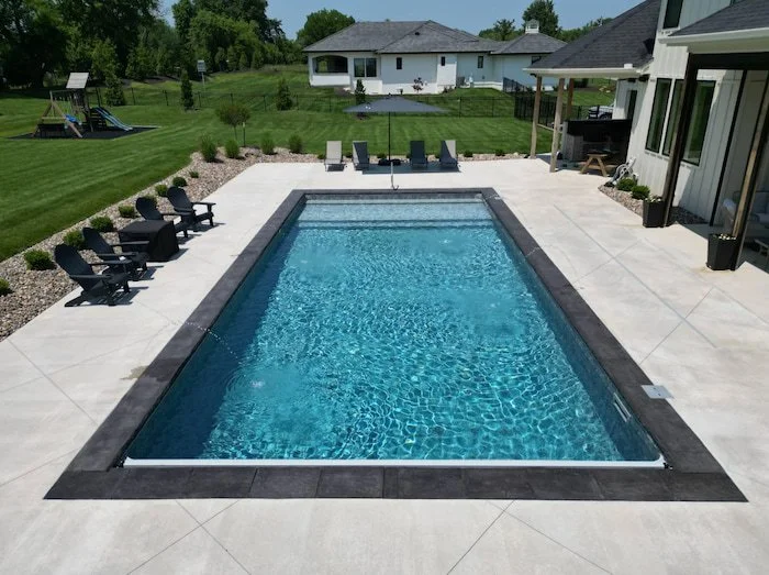 Elevated view of a 20x40 vinyl liner inground pool with an Island Granite liner, slate-colored coping, automatic safety cover with stone lid, and five deck jets, surrounded by a large concrete pool deck with Adirondack seating.