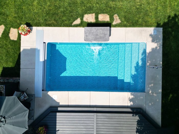 Top-down view of a 10x20 Recreational personal plunge pool with an Azure Mosaic Borderless liner, 4-foot water feature wall in active flow, a wide stair entry, and an automatic safety cover housing.