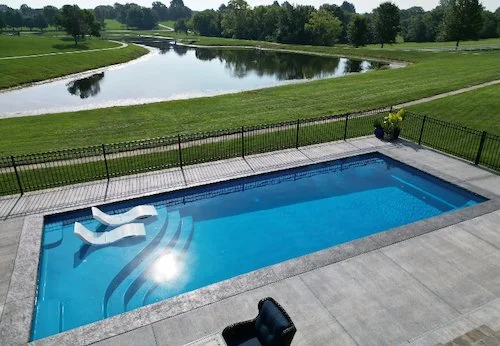 A 16x40 fiberglass inground pool with tanning ledge chairs and decorative coping, installed by Tiger Pool and Patio — Kansas City's trusted pool contractor.