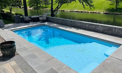 Tiger Pool and Patio fiberglass inground pool installation in Kansas City — Thursday Pools Aspen 12x25 in Caribbean Sparkle with automatic safety cover and large retaining walls overlooking a pond.
