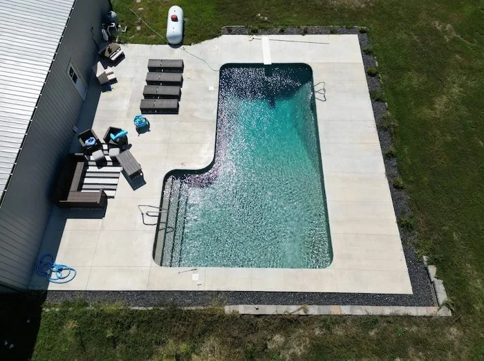 Wide aerial view of a Tiger Pool and Patio 16x40x16x26 L-shaped diver inground pool with GLI Sedona liner and sand gunite, featuring a diving board, full-length steps, a figure four handrail, and a deep end ladder.