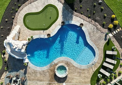 Aerial view of a custom vinyl liner inground pool by Tiger Pool and Patio in Kansas City—20x42 lagoon design with a water slide, standalone spa, putting green, tanning ledge, and turf lounge area.